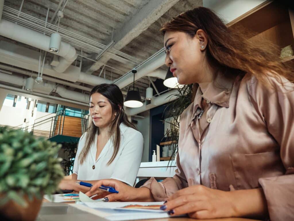 Two women collaborating at a desk in a modern office space, focusing on work tasks.